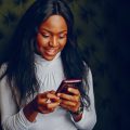 young and beautiful dark-skinned girl in a gray sweater sitting in a cafe at the table and using the phone